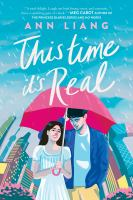 The cover of This Time it's Real. Two teens walk under a red umbrella in the rain, with the Beijing landscape behind them. The teen girl holds the umbrella; she has dark hair, pale skin, and wears a white dress. The teen boy stands close to her under it; he has dark hair, pale skin, and wears a blue jacket, white shirt, and yellow pants. 